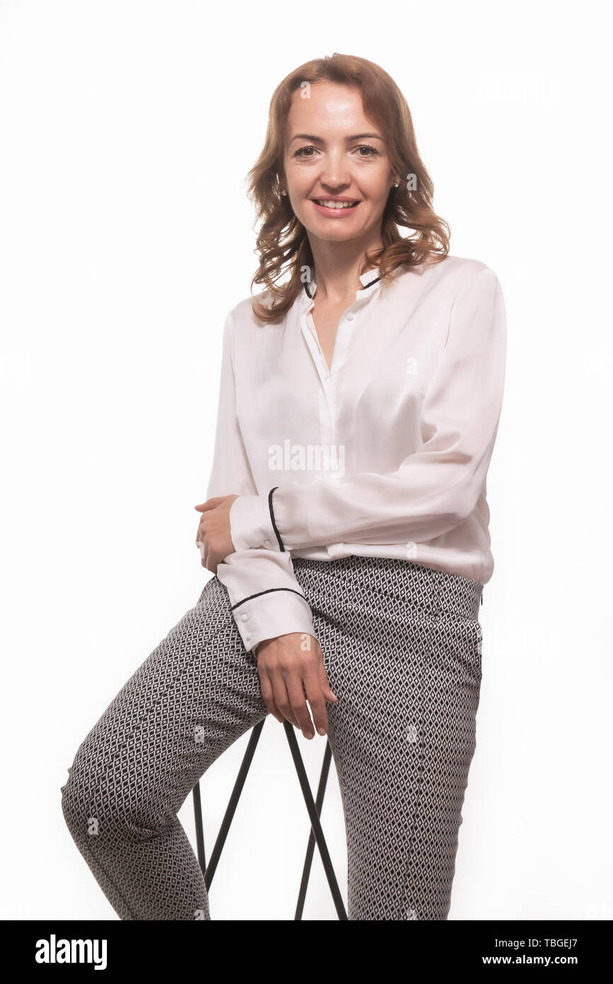 One mature woman, 40 years old, businesswoman portrait posing, leaning on a bar stool. White background behind. Stock Photo