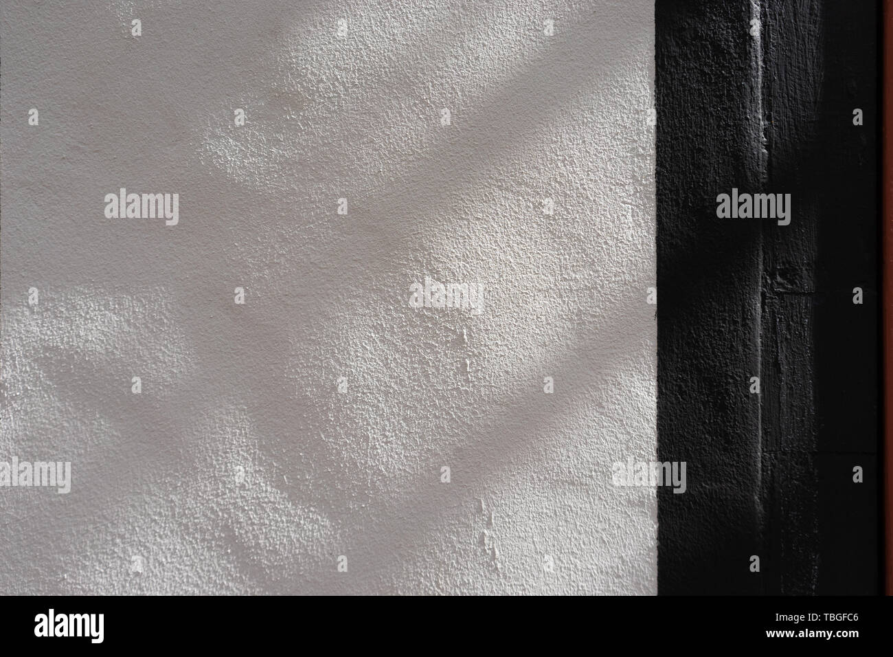 Black stripe on painted white textured wall with shadows on a sunny day