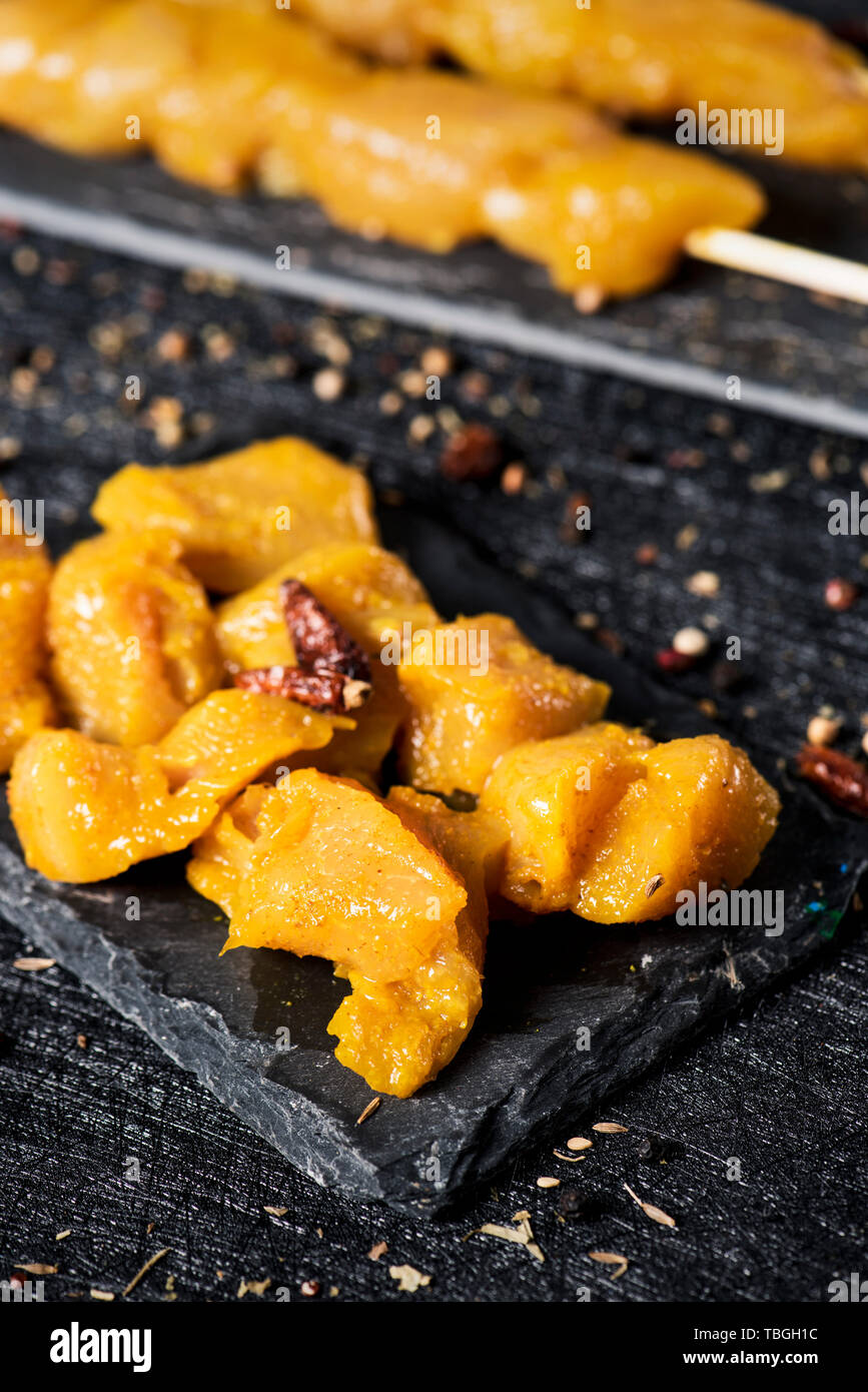 closeup of some spiced raw chicken meat skewers and some dices of spiced raw chicken meat on two black slate plates, on a textile black surface, sprin Stock Photo