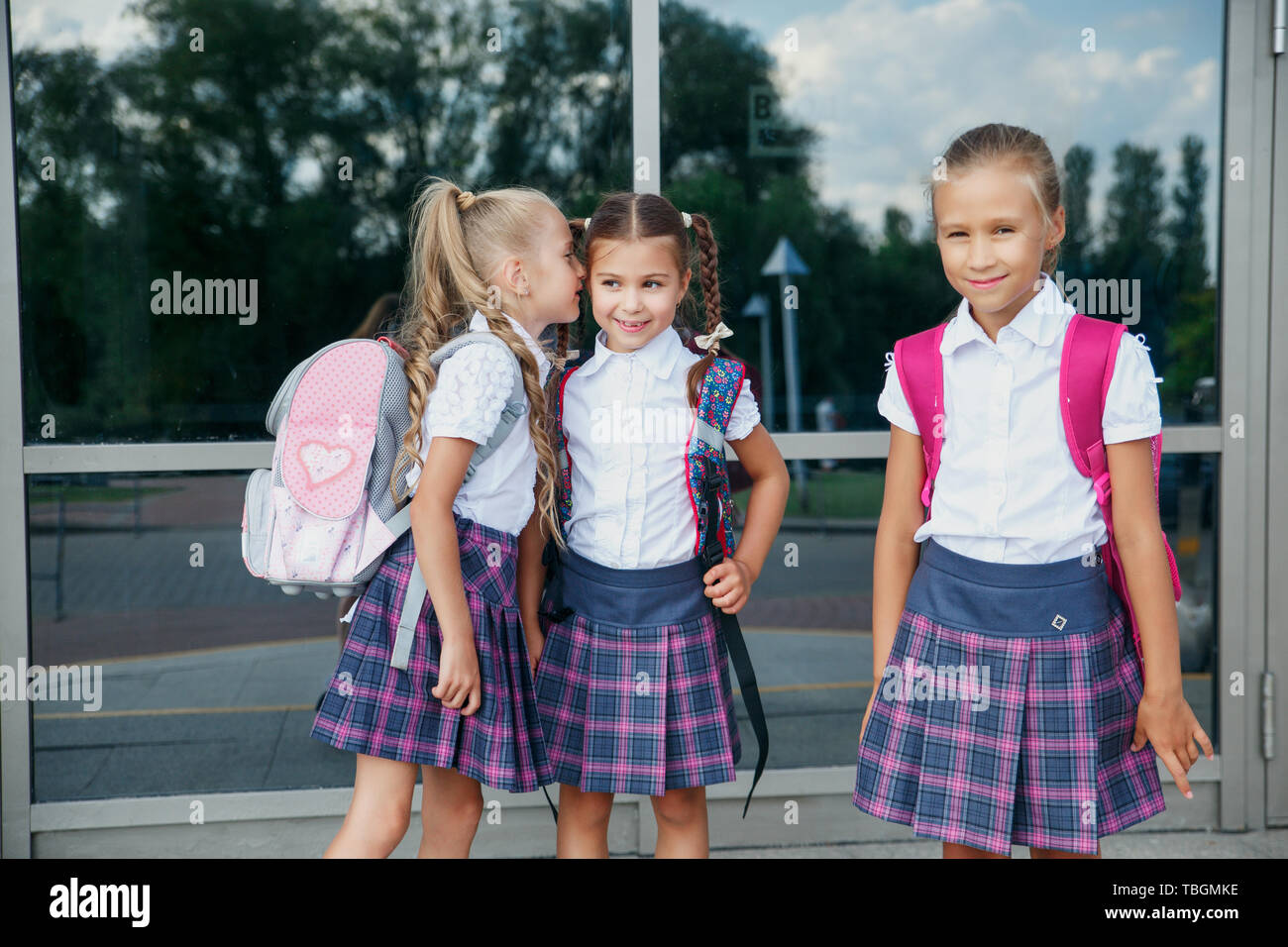 Pupils of primary school. Girls with backpacks near building outdoors. Beginning of lessons. First day of fall. Stock Photo