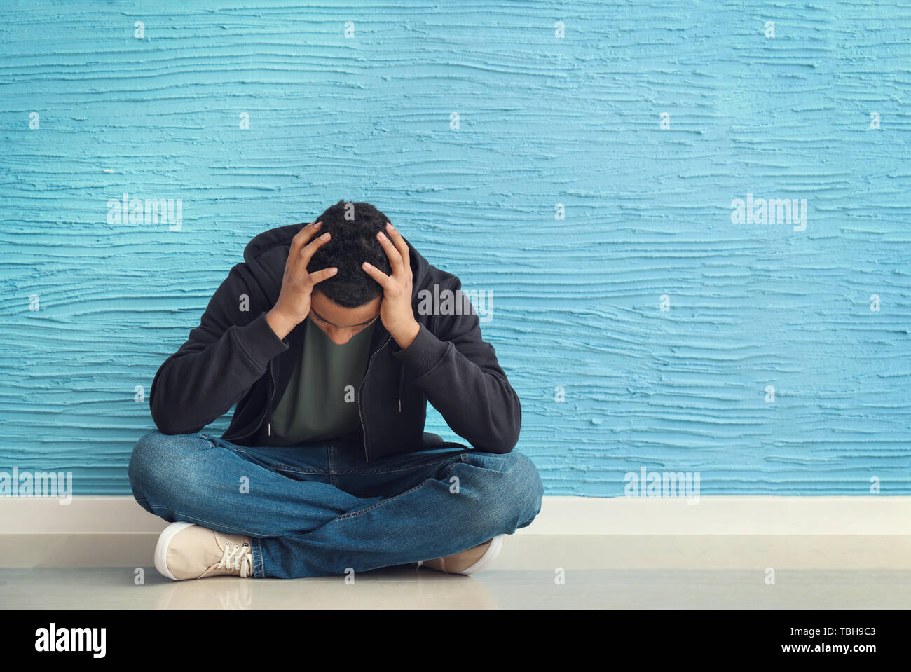 Sad African-American teenage boy sitting on floor near color wall Stock ...