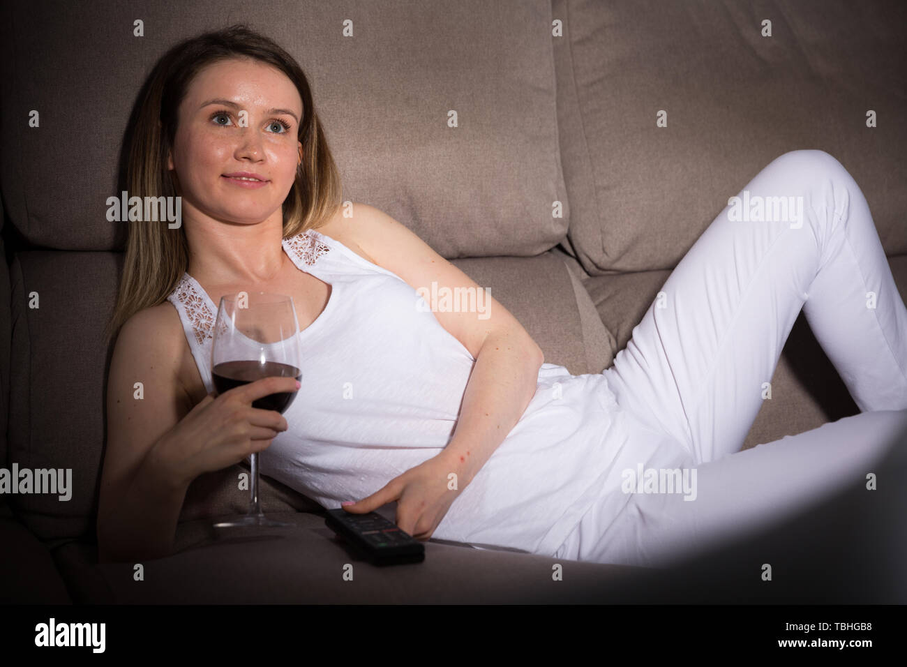 Young woman is sitting with white wine and watching TV at home Stock ...
