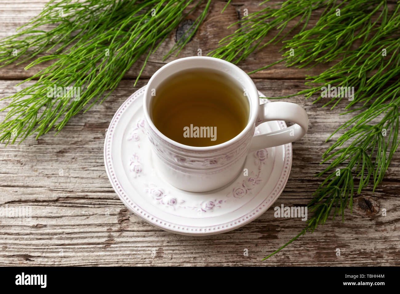 A cup of horsetail tea with fresh Equisetum arvense plant on a table Stock Photo