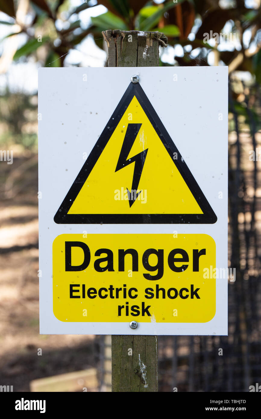 White Electric Fence Hazard Warning Sign with text Danger Electric Shock Risk on a Farm Outside Stock Photo