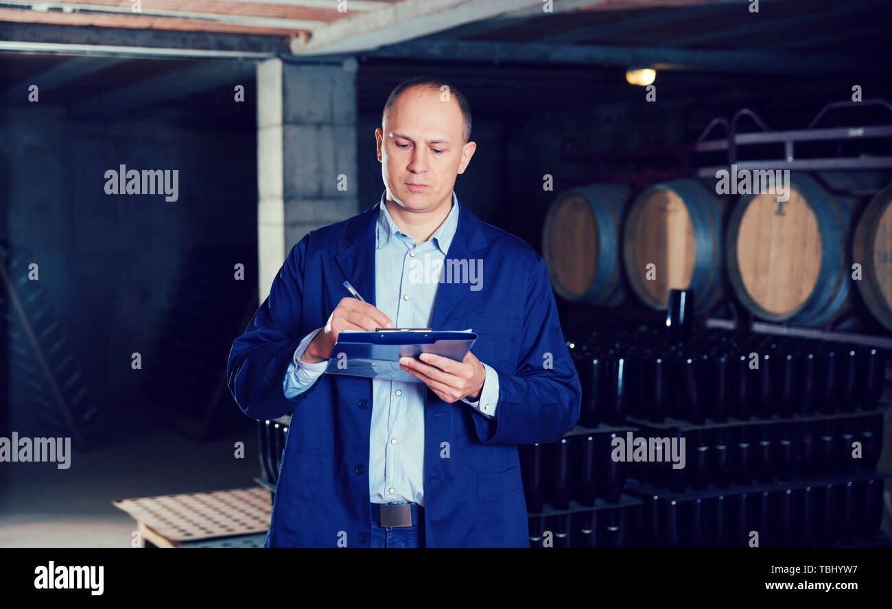 Confident male winemaker working in wine cellar, taking notes on clipboard Stock Photo