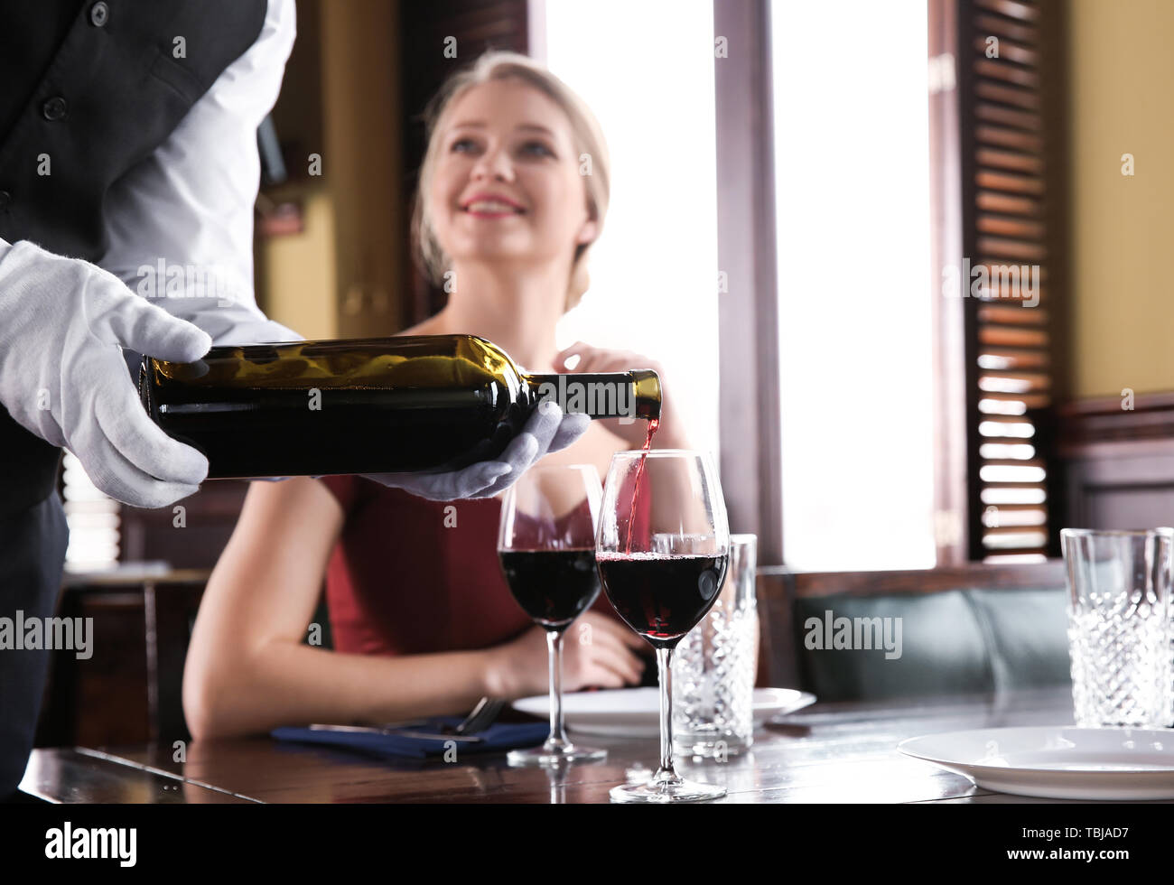 Waiter pouring wine in glasses for clients in restaurant Stock Photo