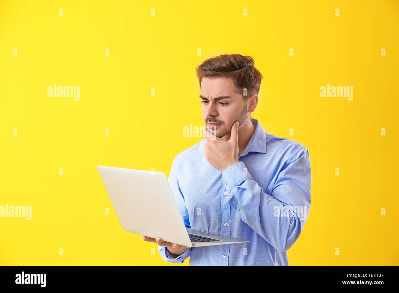 Thoughtful male programmer with laptop on color background Stock Photo