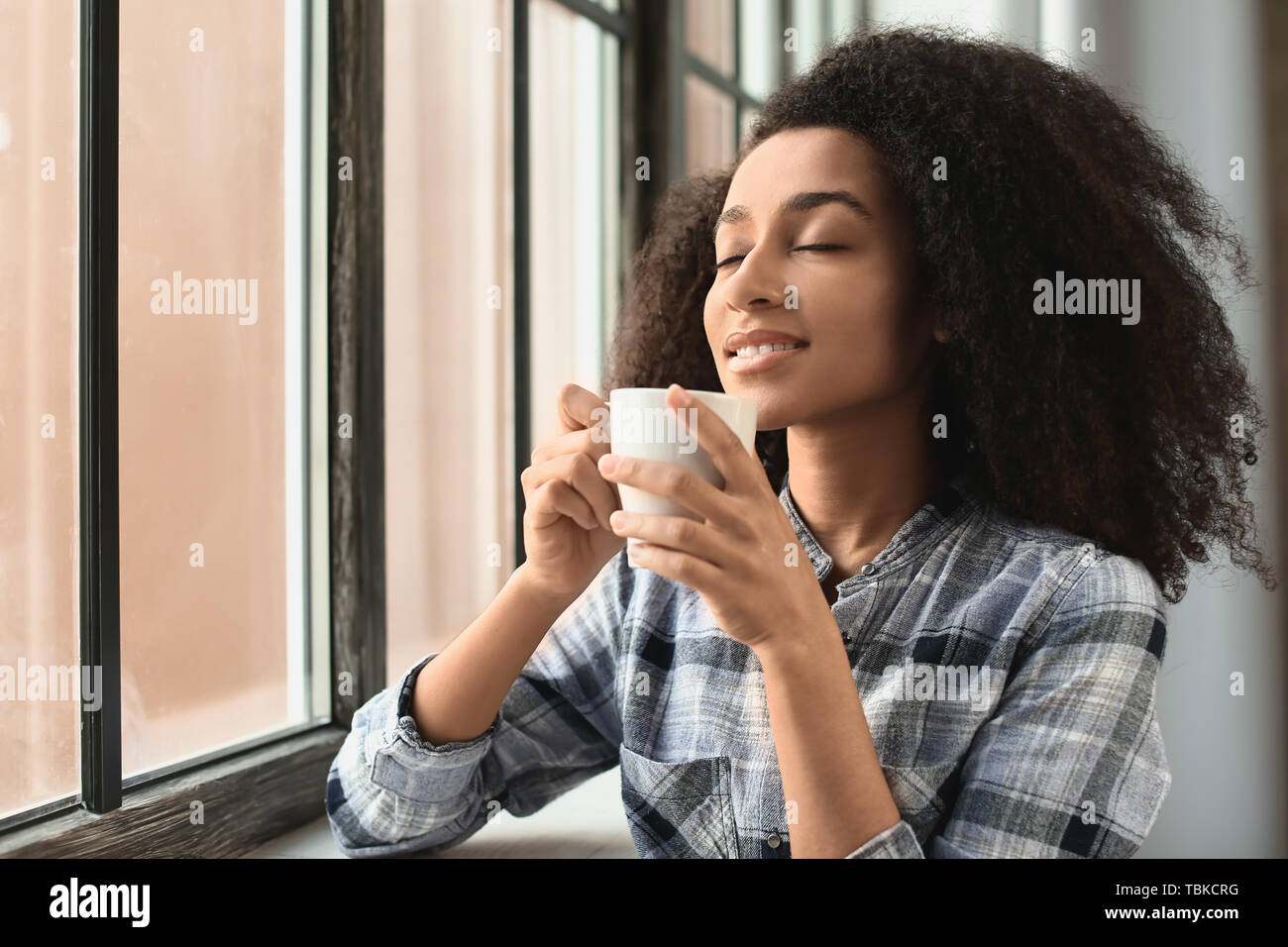 Beautiful African-American woman drinking coffee near window Stock ...
