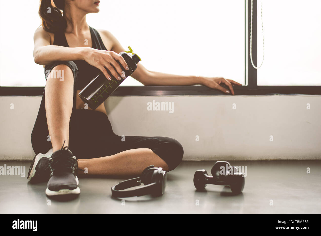 Woman with dumbbell and device exercise lifestyle workout in gym fitness breaking relax after sport training with protein shake bottle background. Hea Stock Photo