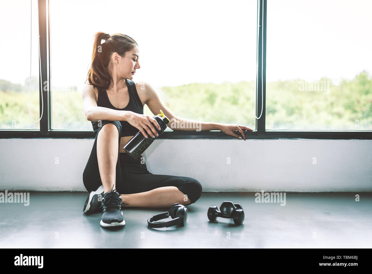 Woman with dumbbell and device exercise lifestyle workout in gym fitness breaking relax after sport training with protein shake bottle background. Hea Stock Photo