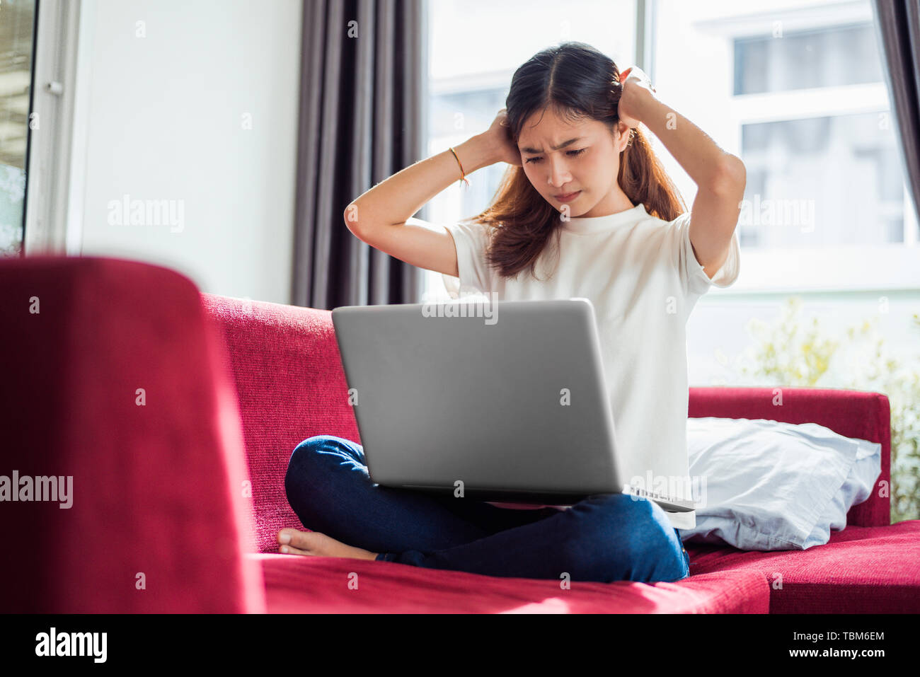 Asian young exhausted businesswoman having headache while using laptop on  sofa in her house. Business people worry and stress about job deadline conc Stock Photo