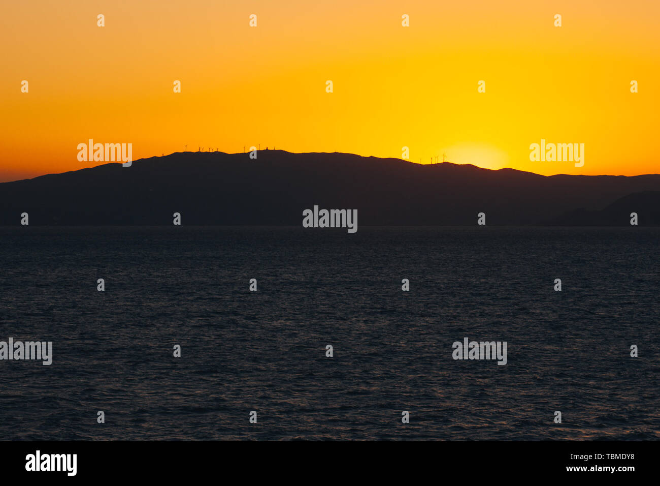 Sun setting behind the profile of an island carpeted with wind turbines Stock Photo