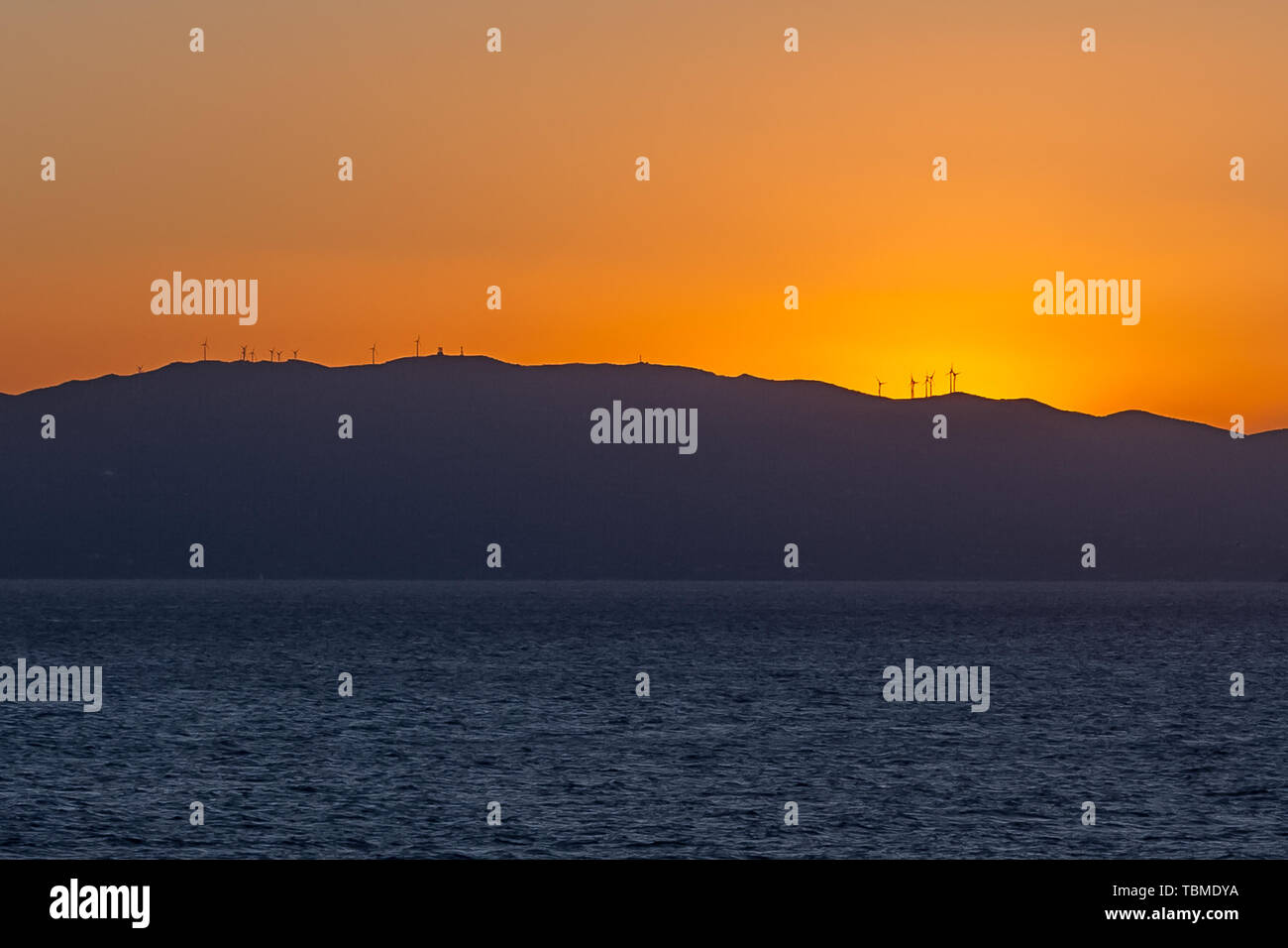 Sun setting behind the profile of an island with wind turbines Stock Photo