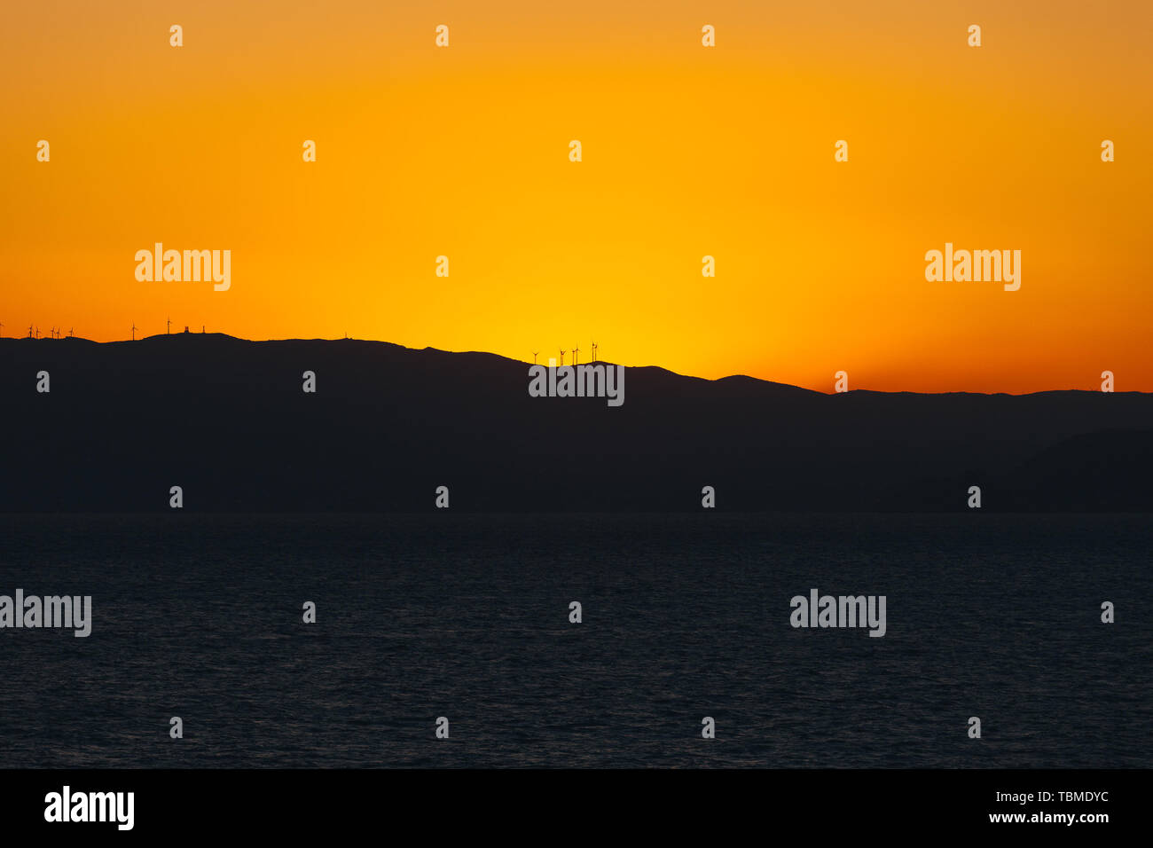 Orange sky behind the profile of an island carpeted with wind turbines Stock Photo