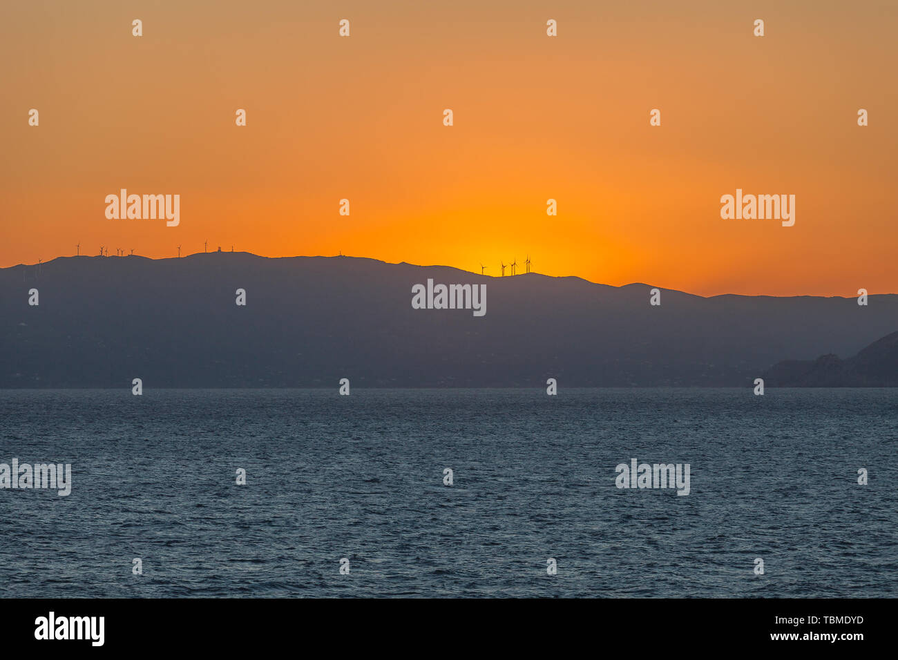 Colorful sky behind the profile of an island carpeted with wind turbines Stock Photo