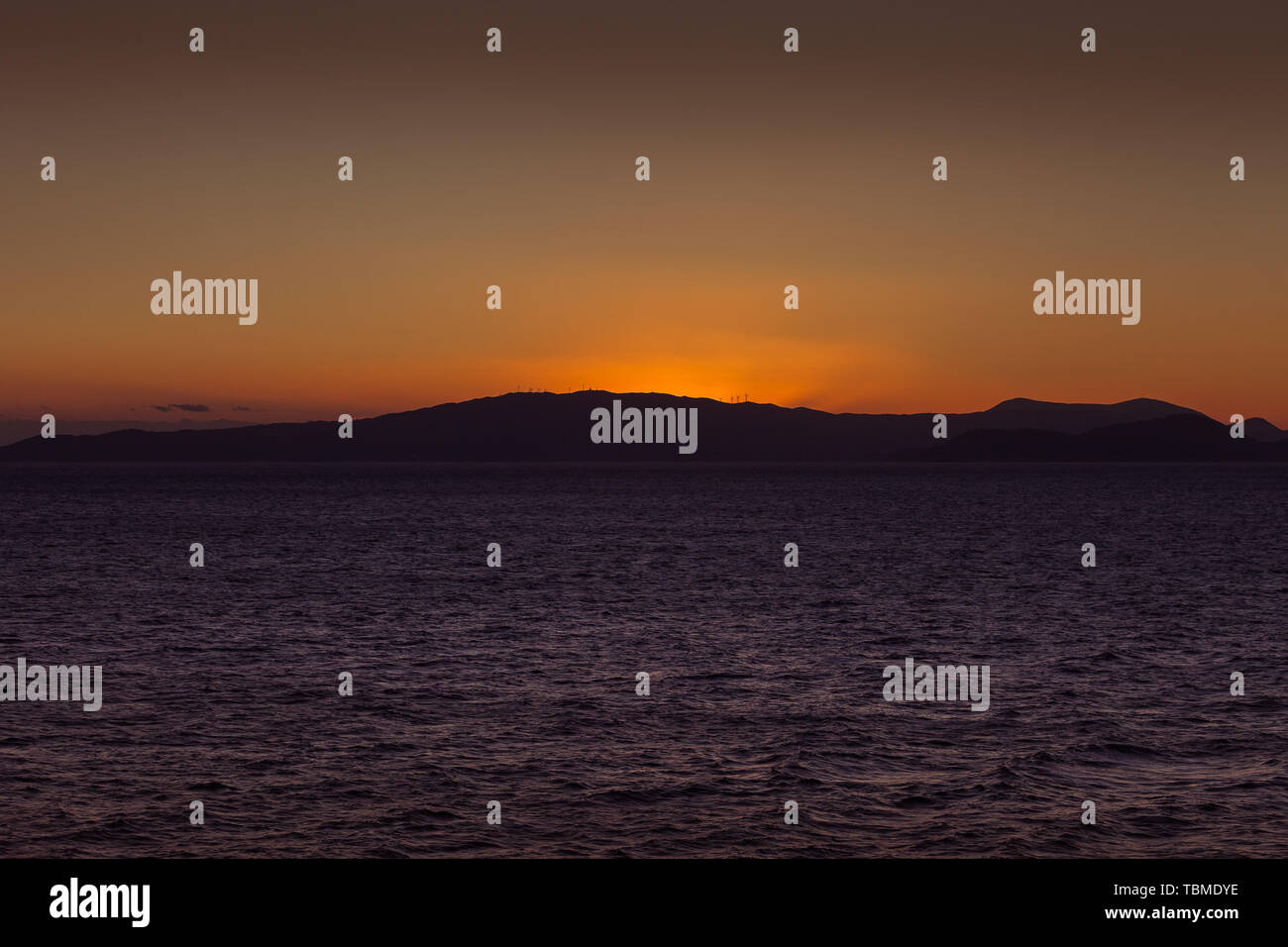 Sun setting behind the profile of island carpeted with wind turbines Stock Photo