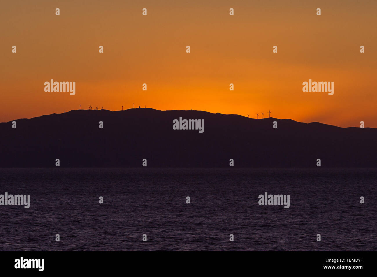 Wonderful orange sky behind the profile of an island carpeted with wind turbines Stock Photo