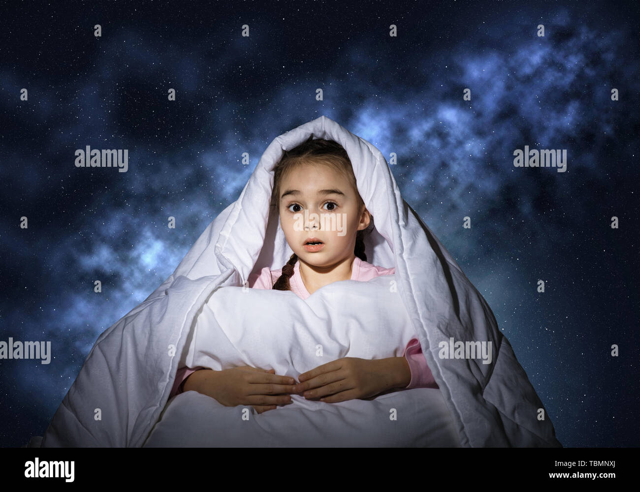 Scared girl with pillow hiding under blanket Stock Photo