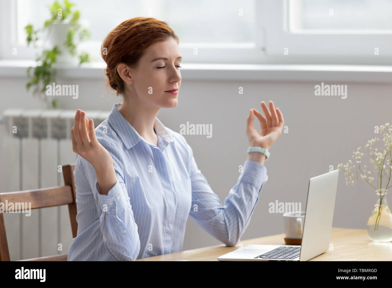 Young pretty businesswoman meditating, doing breathing exercises in office Stock Photo