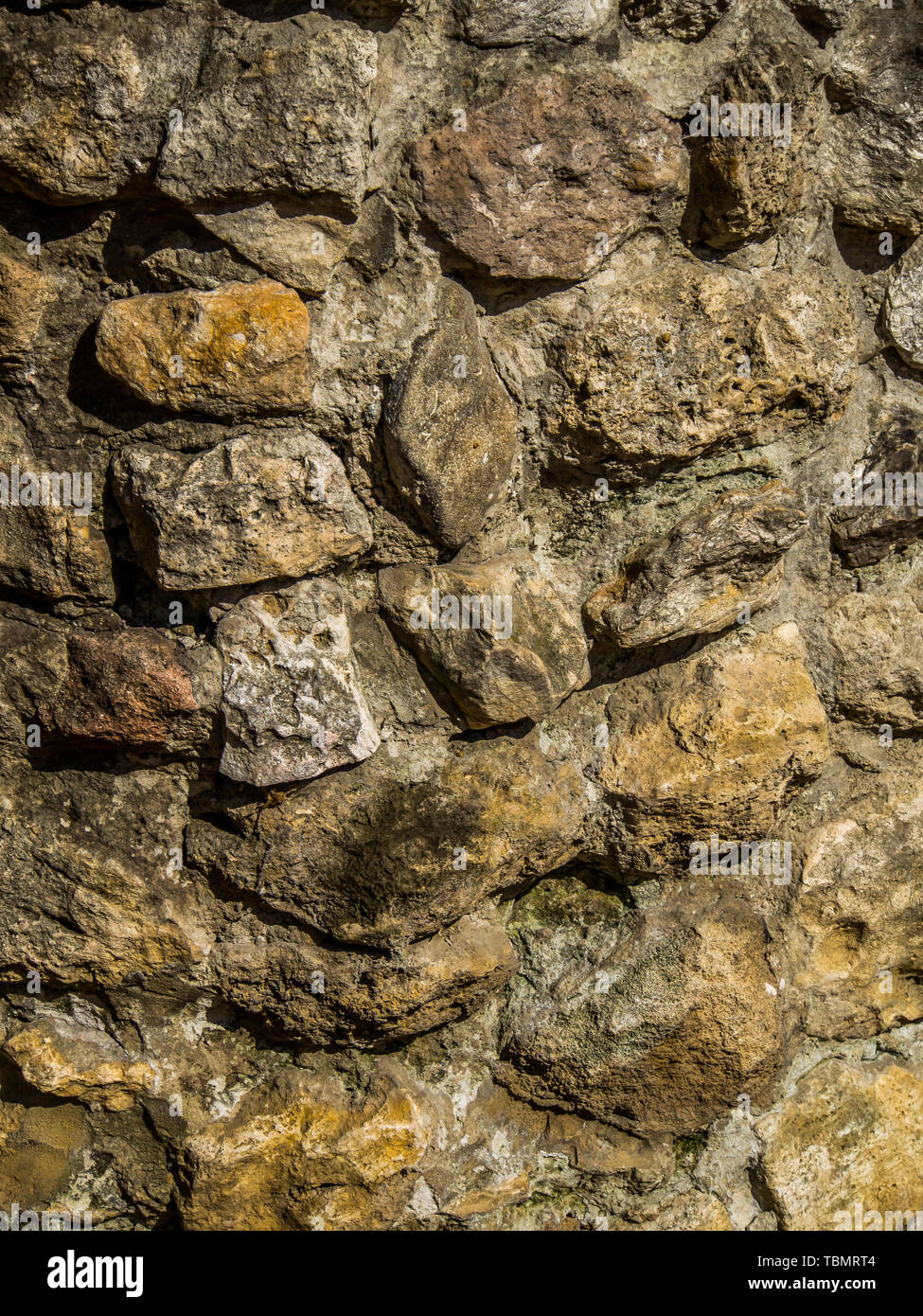 Background. The wall of multi-coloured stones agglomerated with cement mortar Stock Photo