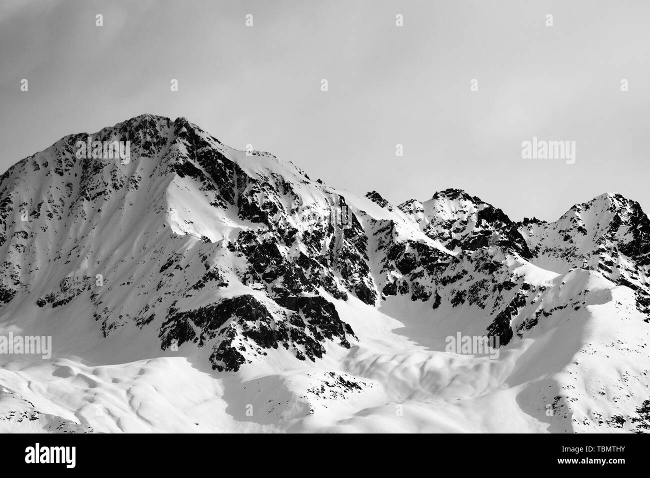 Black and white view on snowy sunlight mountain and gray sky in winter evening. Caucasus Mountains. Svaneti region of Georgia. Stock Photo