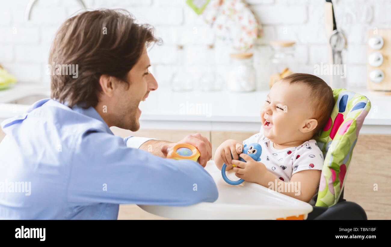 Millennial man laughing with his baby son in kitchen Stock Photo