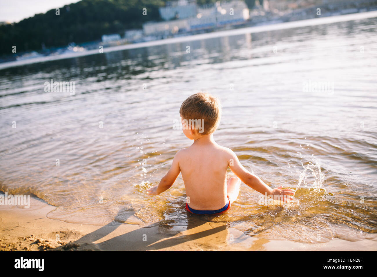 Theme is summer time and rest near the water. Little joyful Caucasian funny boy plays and enjoys in the river. The child is resting and swimming in Stock Photo