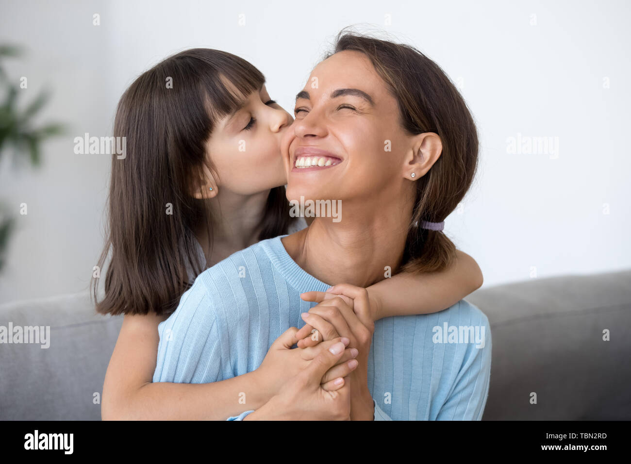 Cute little daughter kiss happy mom on cheek Stock Photo