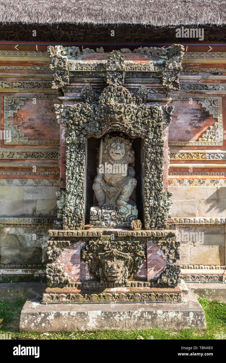 Ubud, Bali, Indonesia - February 26, 2019: Batuan Temple. Niche with lion-like figure holding sword. Red bricks and gray stone ornaments covered with  Stock Photo