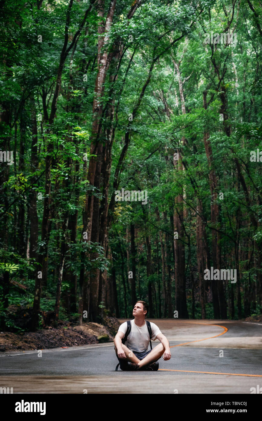 Man with backpack sits on road through green Bilar Man-Made Forest, Bohol, Philippines Stock Photo