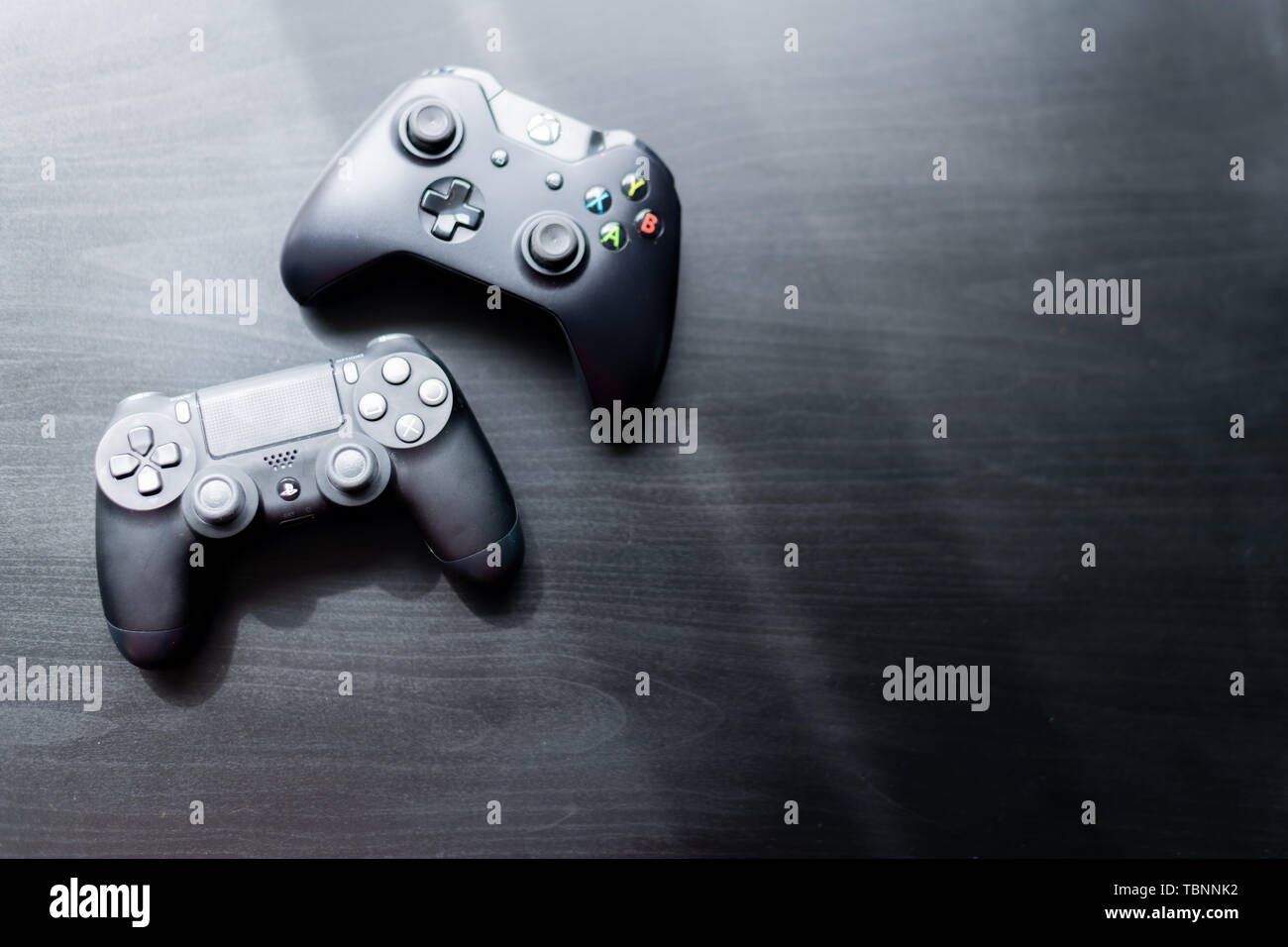 Xbox and Playstation controller sat next to each other on a dark background Stock Photo
