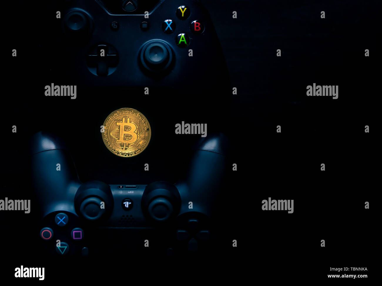 Playstation and Xbox controllers next to a physical Bitcoin. Stock Photo