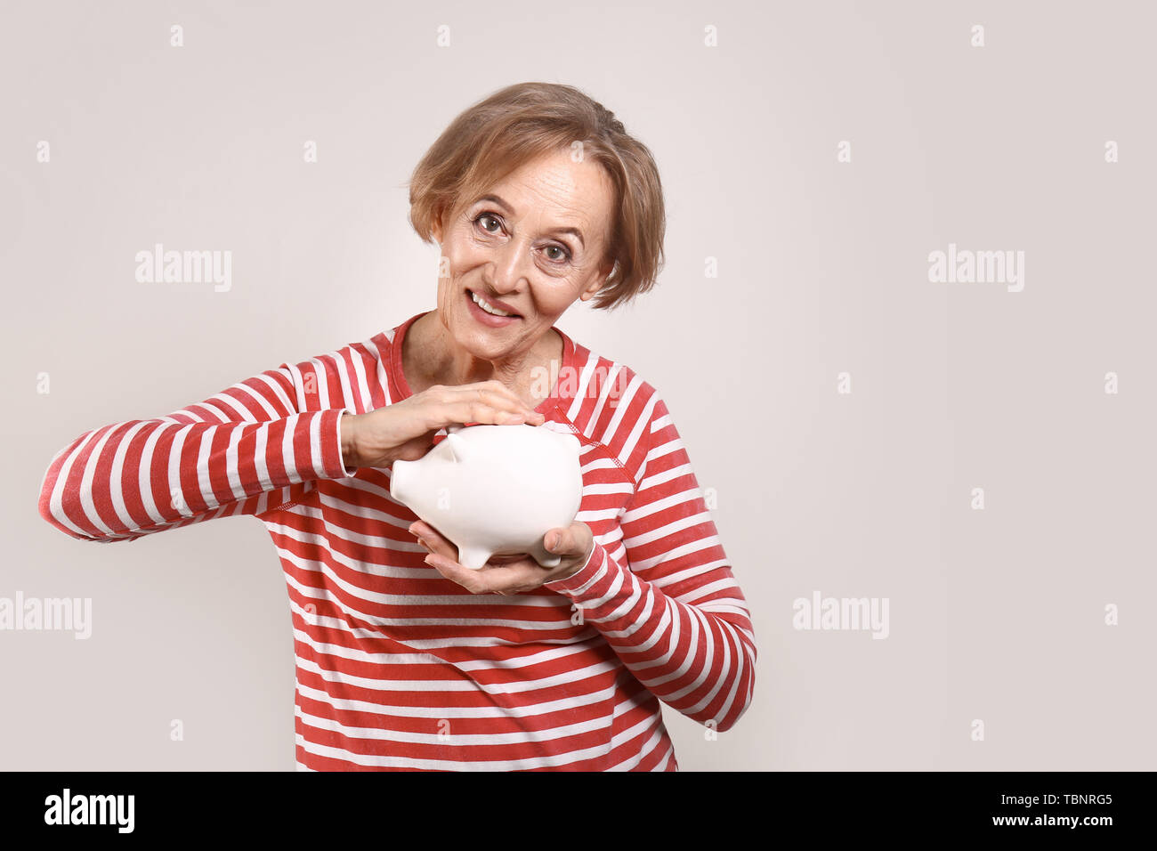 Beautiful mature woman with piggy bank on grey background Stock Photo ...