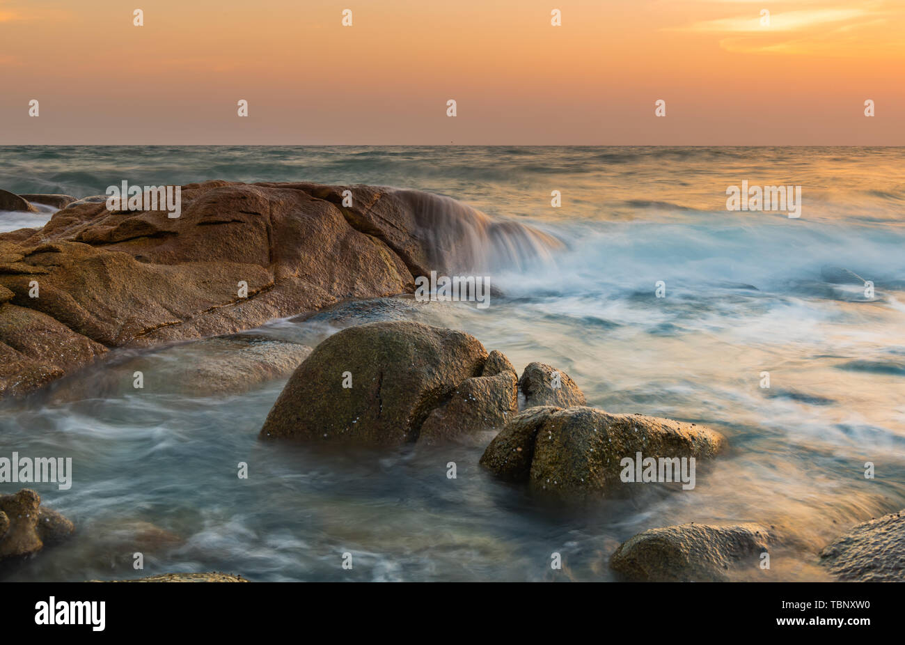 The rock and smooth sea wave in the sunset time photo with outdoor low and dark lighting seascape. Stock Photo