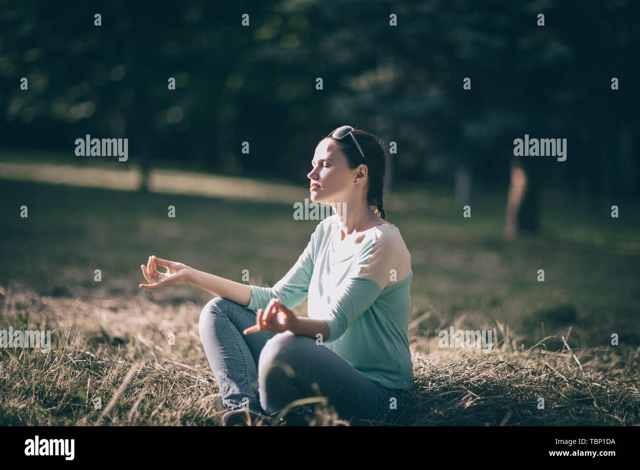 beautiful young woman meditating in Lotus position sitting on the lawn ...