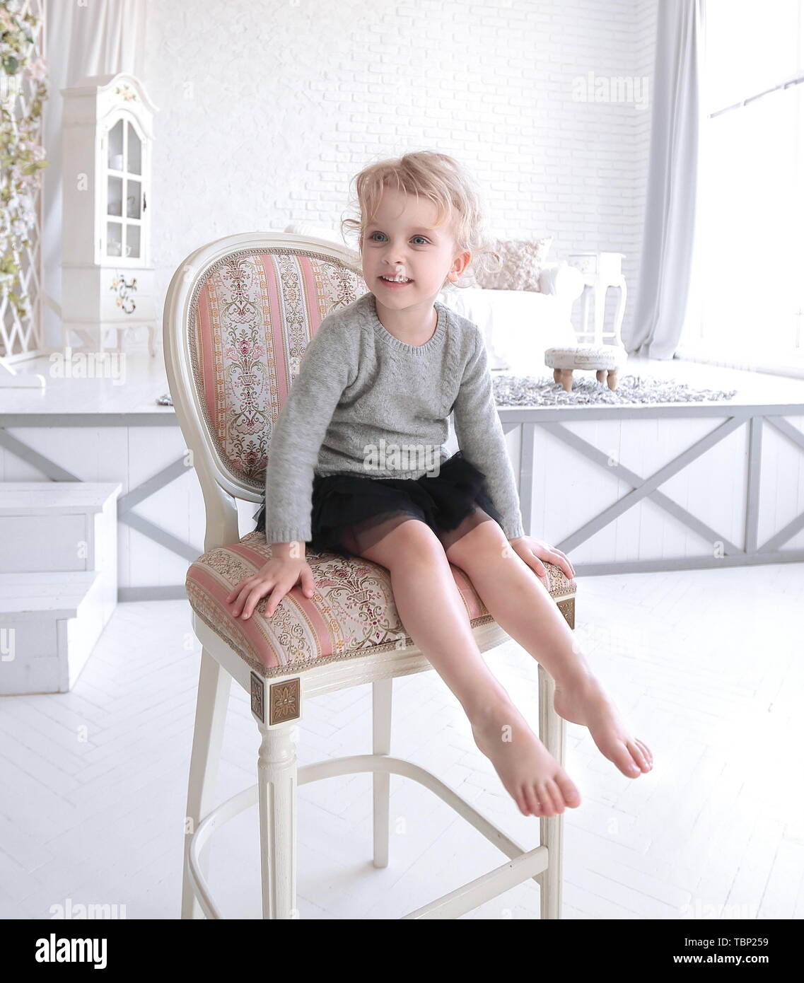 portrait of little girl sitting on a chair in a spacious room Stock ...