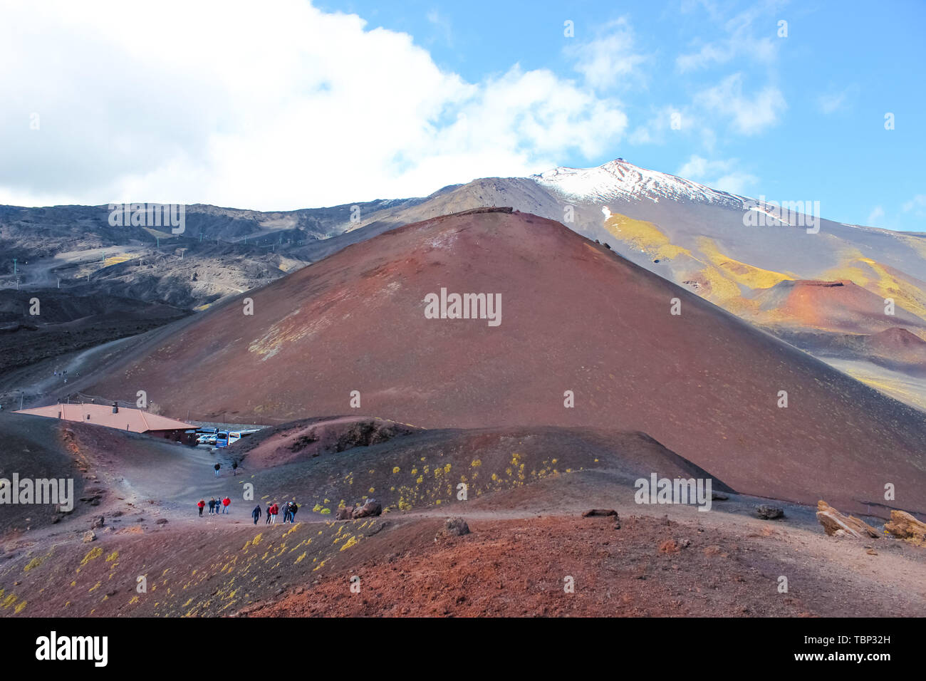 Mount Etna, Sicily, Italy - April 9th 2019: Hikers walking on the Silvestri craters on the Mount Etna. The very top of Etna volcano with snow in the background. Popular tourist spot. Stock Photo
