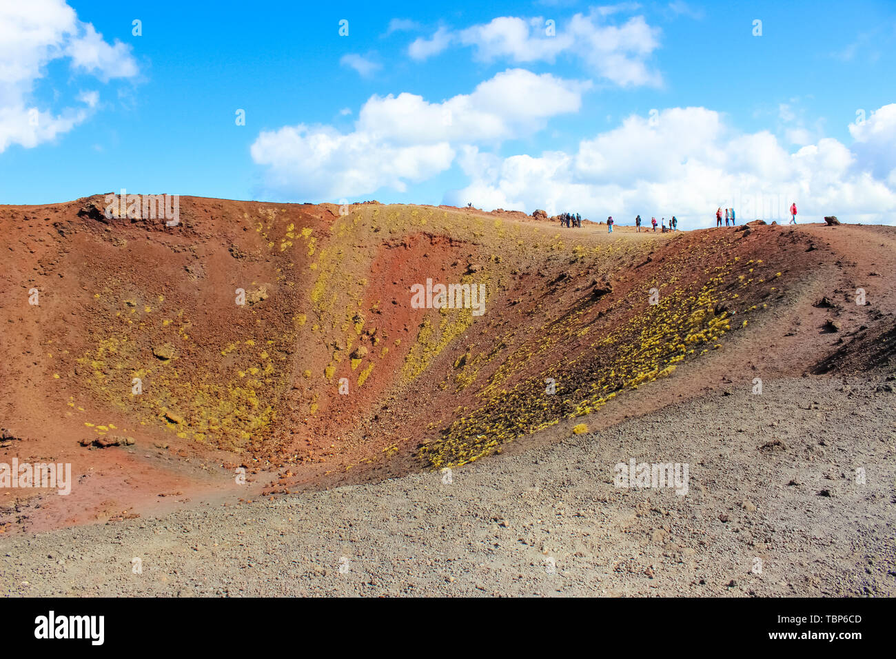People walking around the colorful crater in Silvestri craters on Mount Etna in Sicily, Italy. The stunning volcanic landscape is a popular hiking spot. Stock Photo