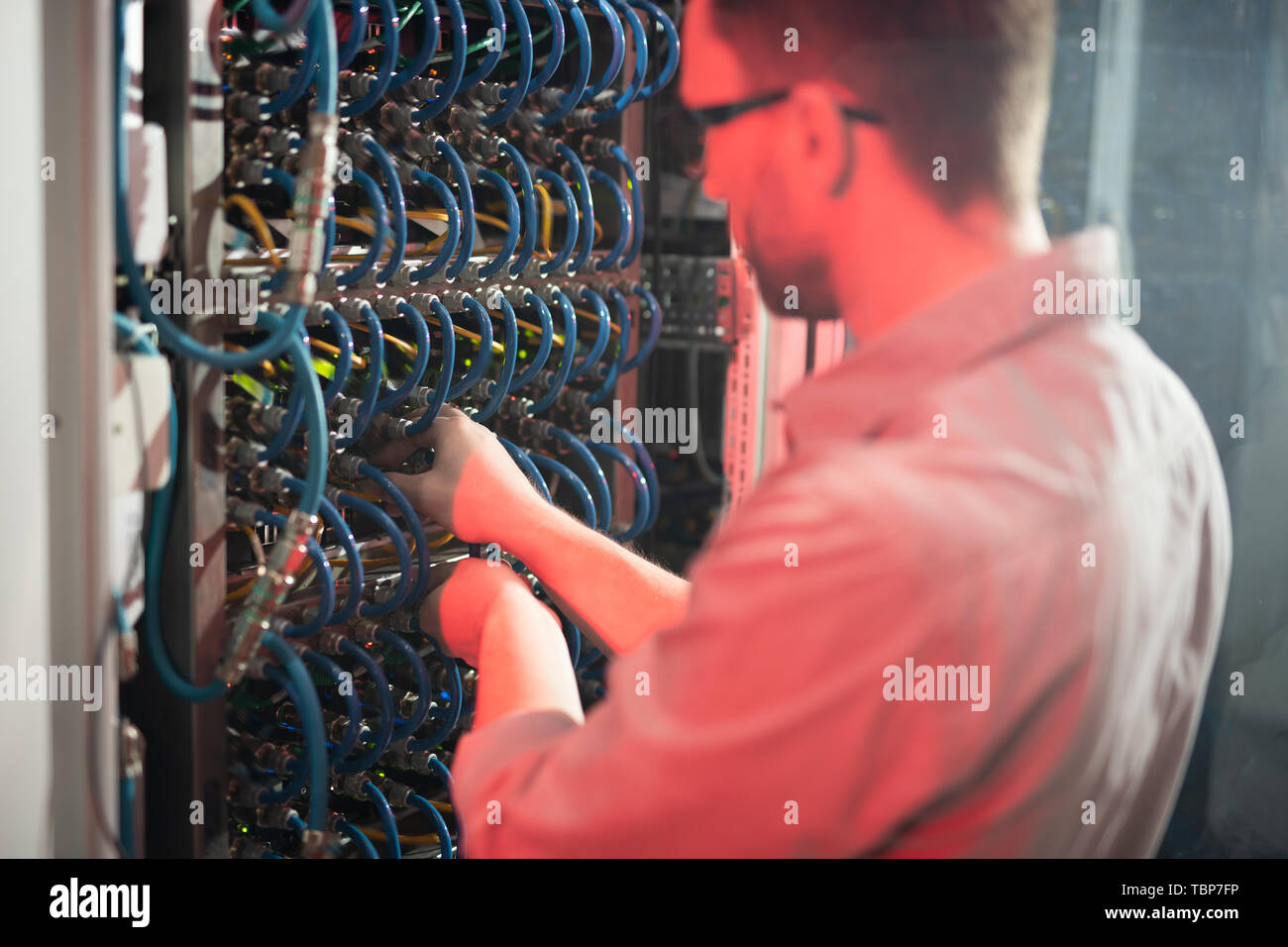 Rear view of skilled man standing by cabinet of server racks and ...