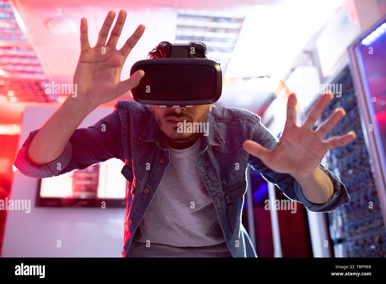 Serious curious young middle-eastern innovation scientist gesturing hands while using virtual reality simulator in database storage room Stock Photo