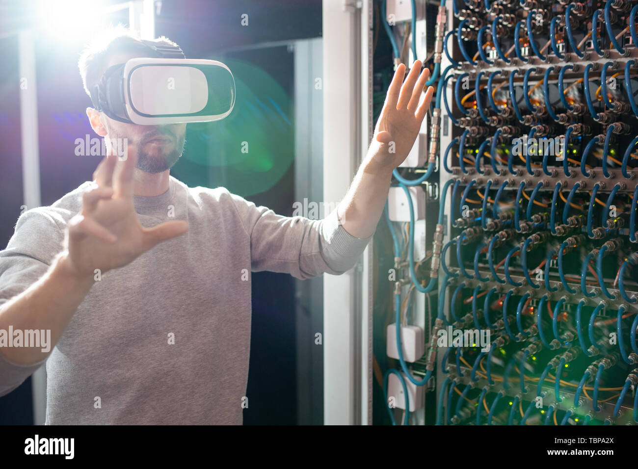 Serious concentrated young bearded engineer in VR goggles standing in database center and gesturing hands while managing server links wirelessly Stock Photo