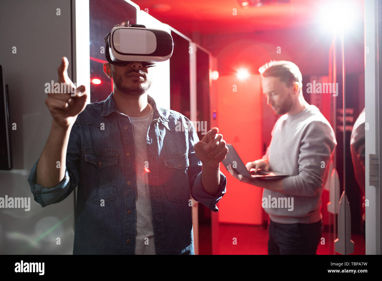Serious hipster young middle-eastern IT scientist pointing with finger and using virtual reality simulator while testing server opportunities in data  Stock Photo