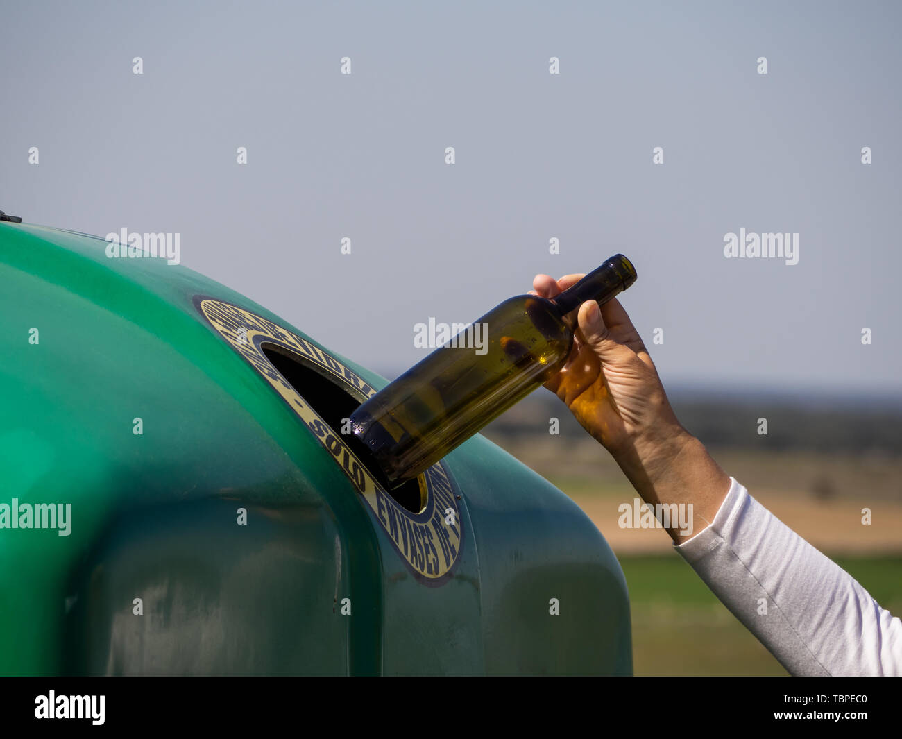 A mature woman pulling a crystal bottle in a green bin for recycling glass with the spanish text 'only glass containers' Stock Photo