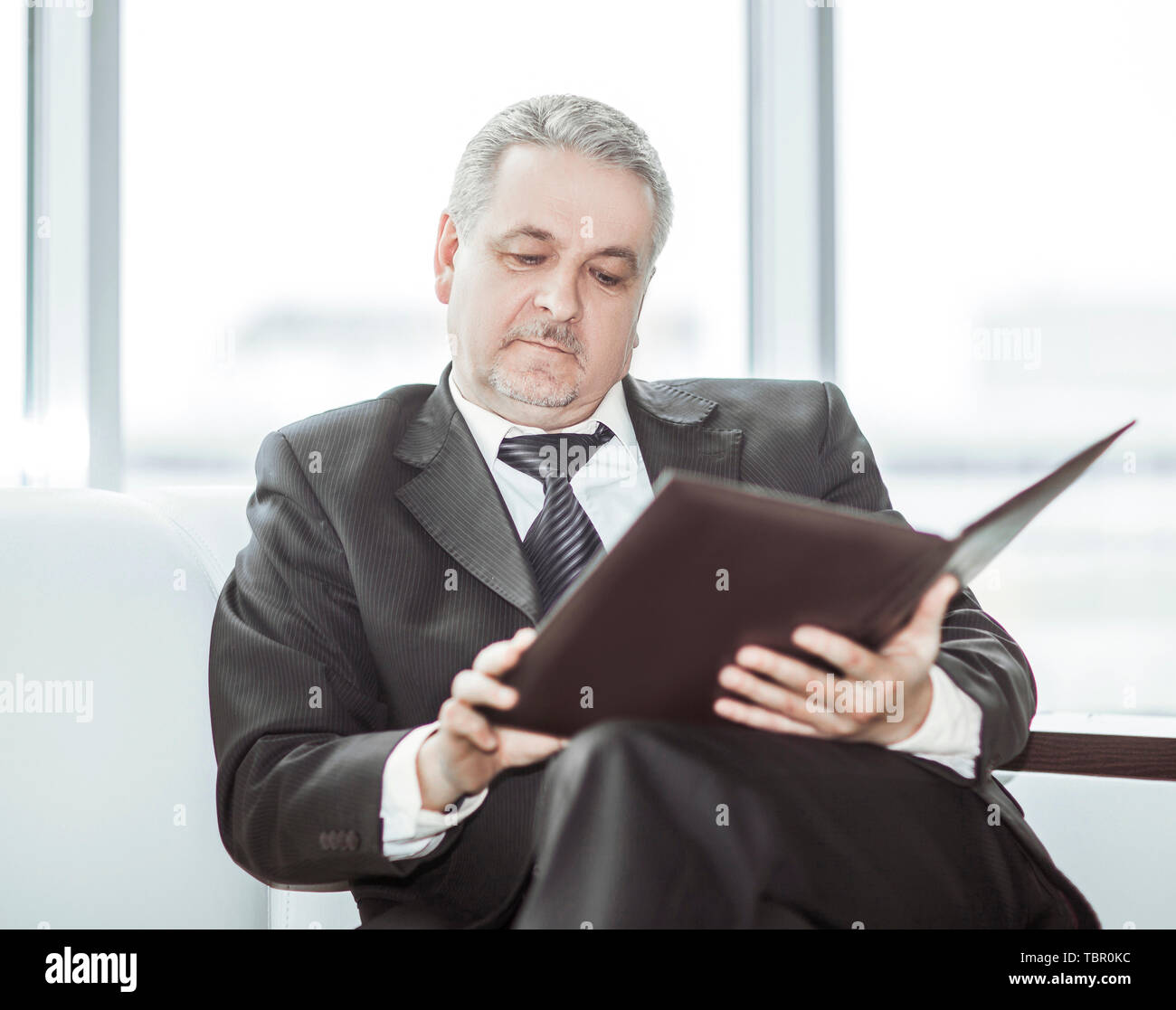 experienced lawyer reviews the documents with the terms of a new contract sitting on the sofa in the private office. Stock Photo