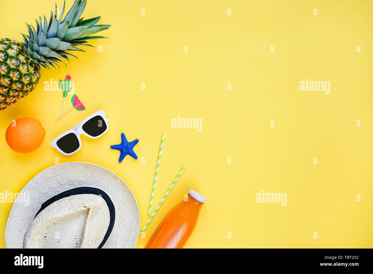 Summer vacation background. Straw hat, white sunglasses, tropical fruits, fresh juice and cocktail accessories over yellow background. Copy space, fla Stock Photo
