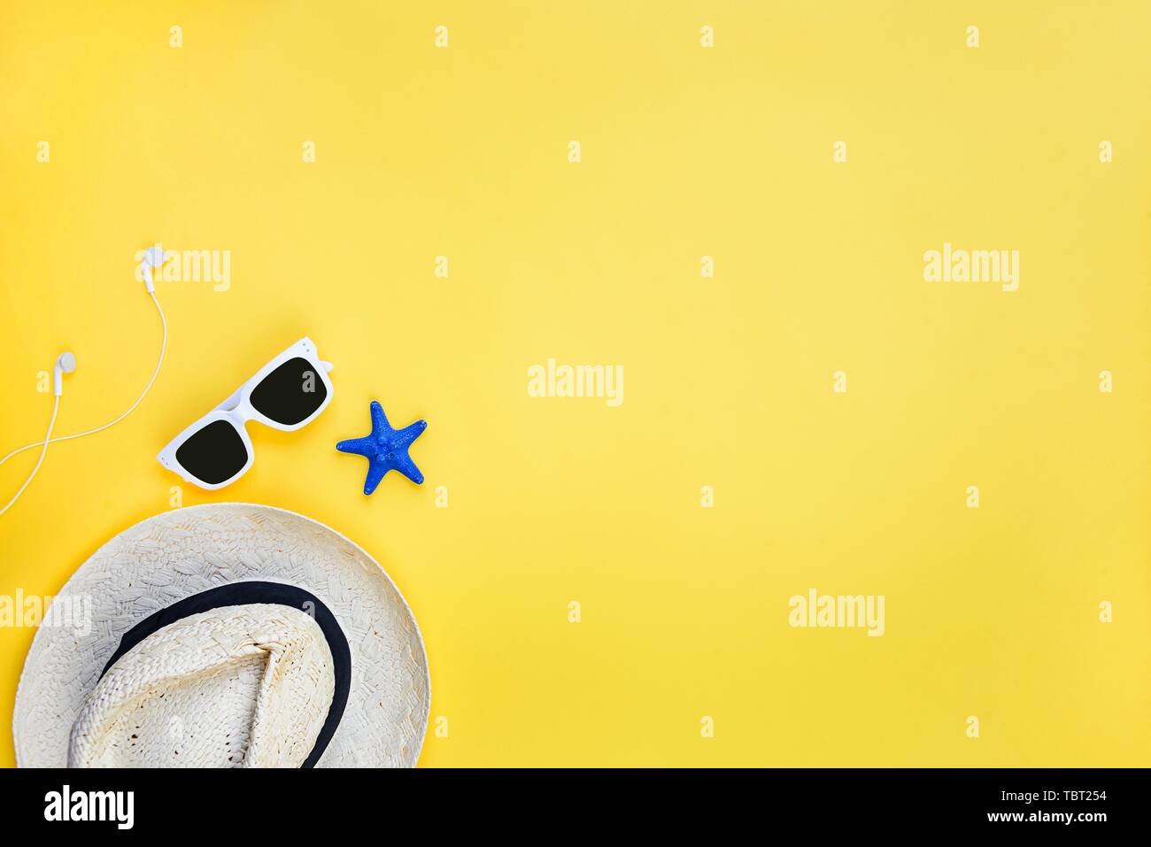 Summer vacation background concept. Straw hat, white sunglasses and earphones over yellow background. Copy space, flat lay. Stock Photo