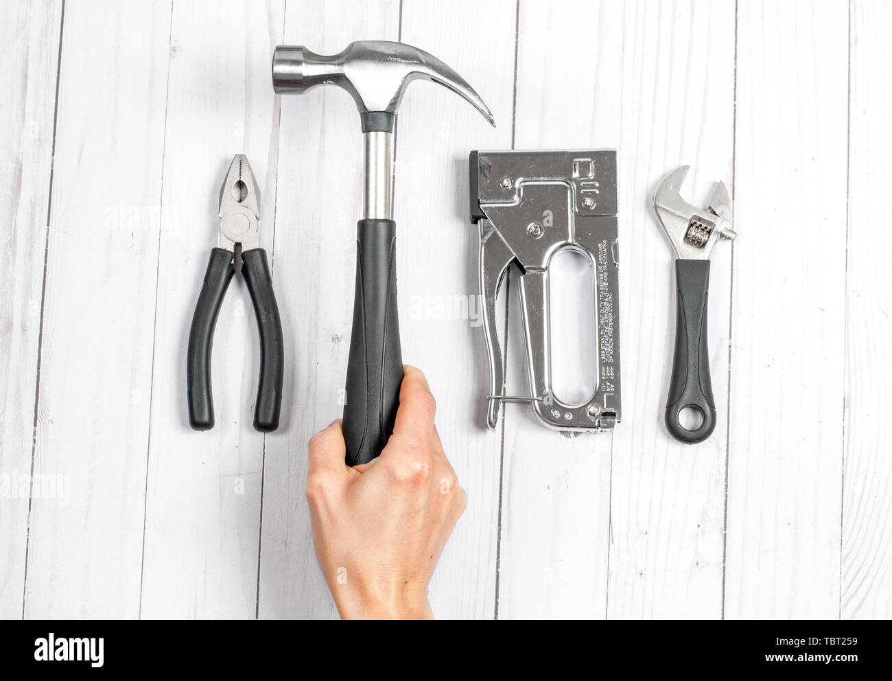 Hand holding hammer. Tools, wrenches and pliers on a white wooden background Stock Photo
