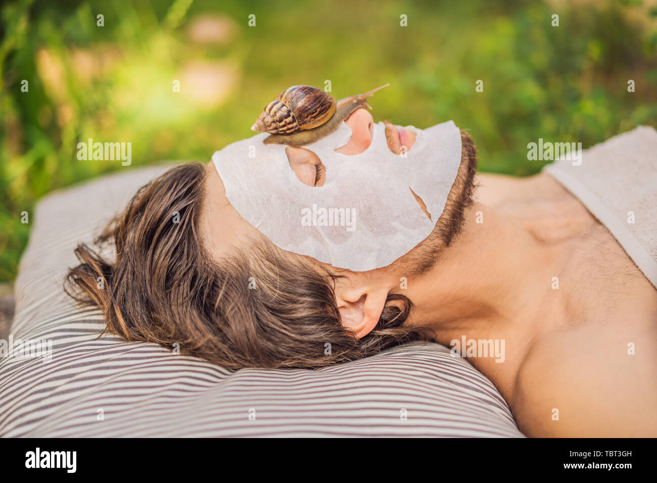 Young man makes a face mask with snail mucus. Snail crawling on a face