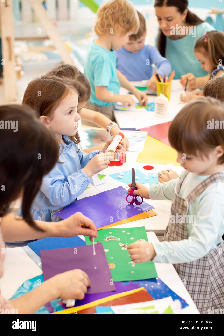 Development learning children in preschool. Children's project in kindergarten. Group of kids and teacher cutting paper and gluing with glue stick on art class in kindergarten or daycare Stock Photo