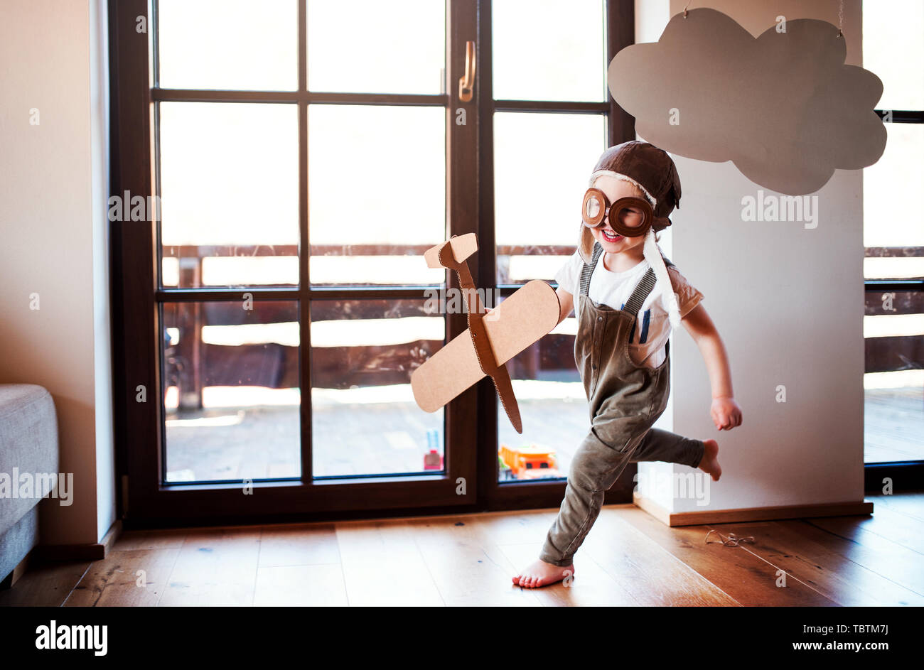 A toddler boy with carton plane playing indoors at home, flying concept. Stock Photo
